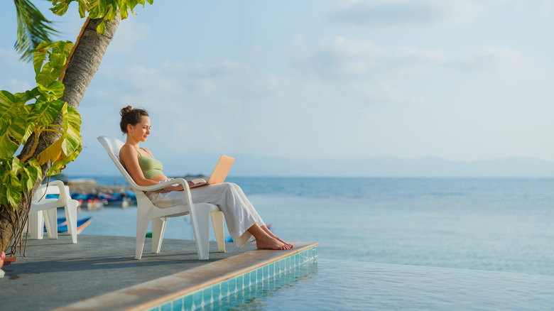 woman using a laptop while sitting by a pool