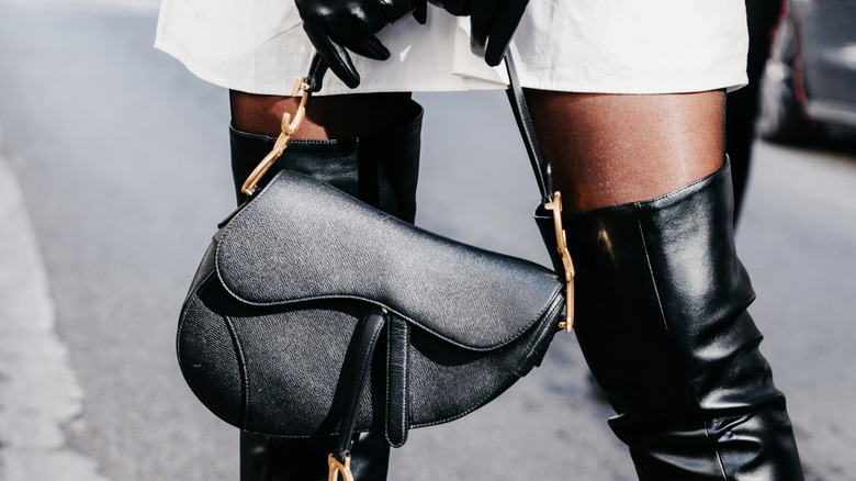 Stylish woman wearing gloves and long boots holding Dior Saddle bag