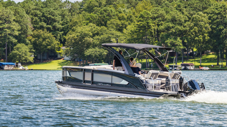 Three people sitting in a pontoon boat on a lake with a forested shoreline in the background