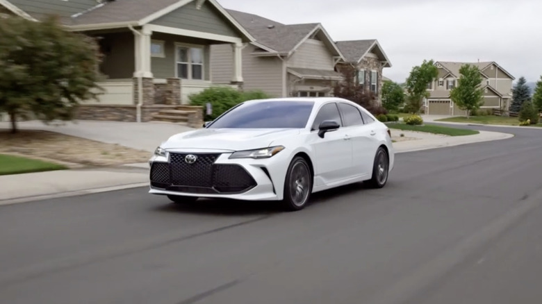 A white 2022 Toyota Avalon driving through a suburban neighborhood