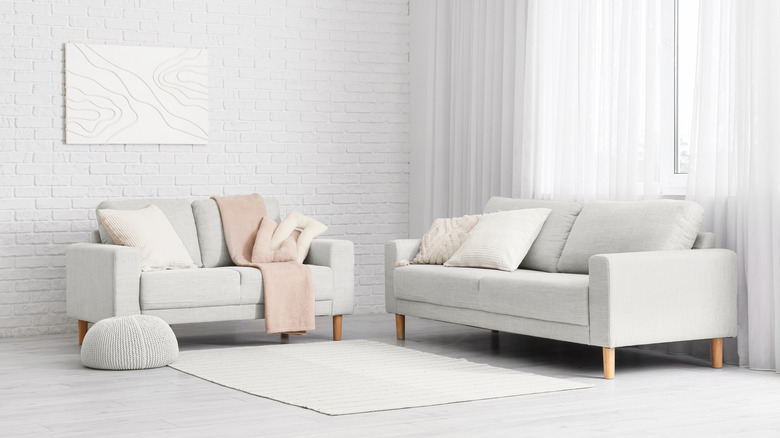 A pair of couches diagonal to each other in front of a white brick wall with an abstract painting on it