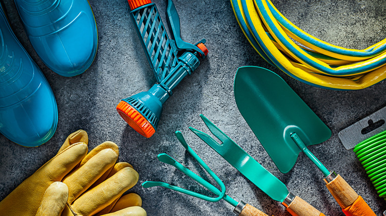 Overhead view of various gardening equipment including a shovel, boots, and a water hose