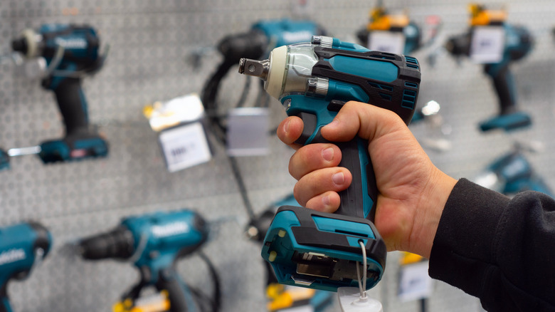 Man holds a power tool in front of a display of power tools
