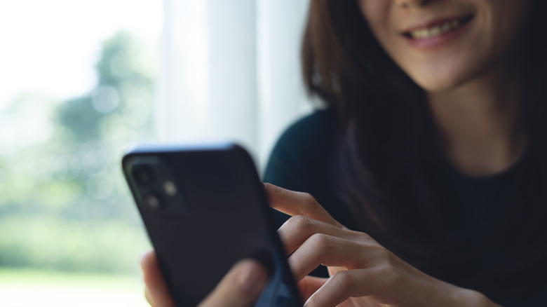 A woman smiles as she touches the screen of a smartphone in her hand