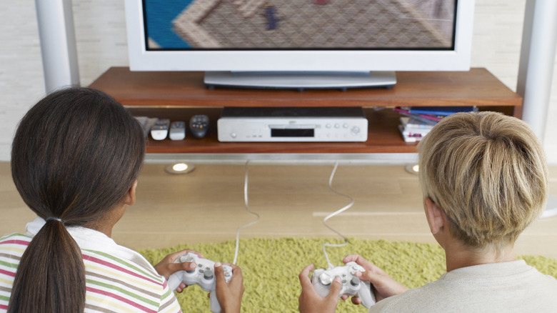 Image of the back of a boy and girl seated playing video games in front of a television.