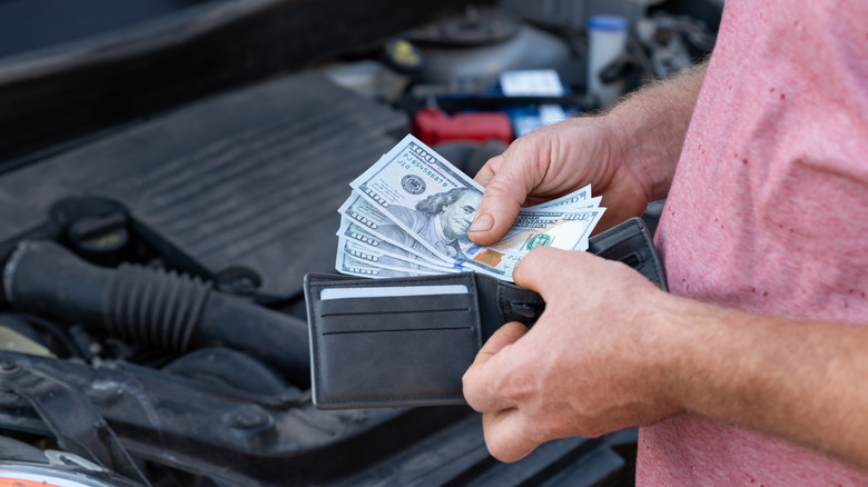Customer taking dollar banknotes of his wallet to pay for car repair.