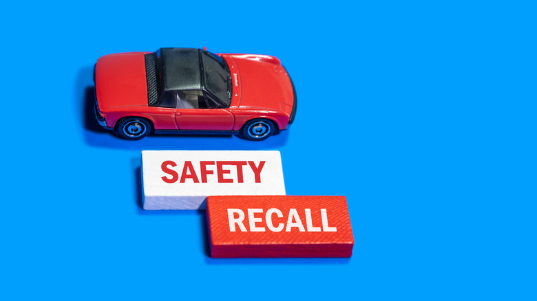 Red toy car with SAFETY RECALL message on blocks against a blue background