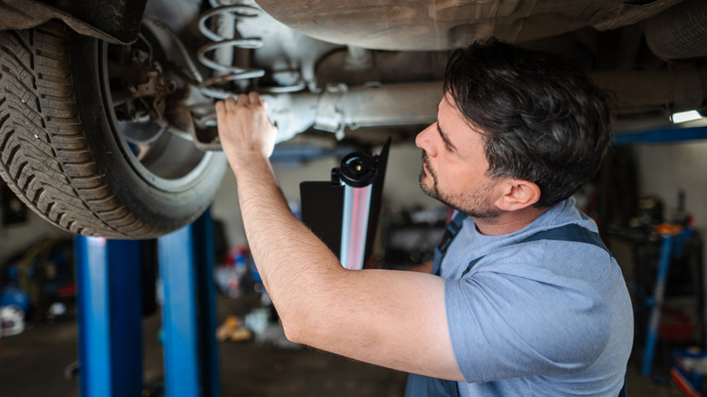 Mid adult mechanic working under a car held up by a hydraulic lift, holding a flashlight