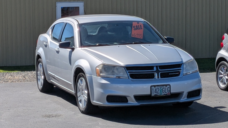 A silver Dodge Avenger sedan with for sale sign parked in a small-town