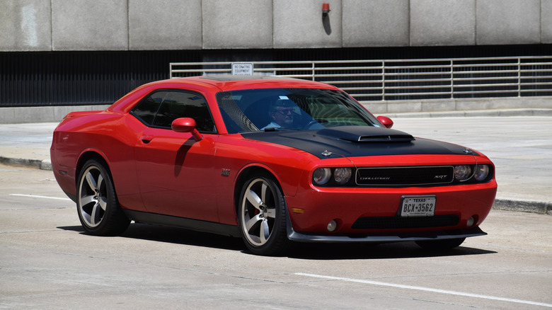 A red and black Dodge Challenger sports car traveling in a downtown district