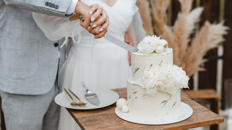 Newly married couple share knife they use to cut a decorative wedding cake