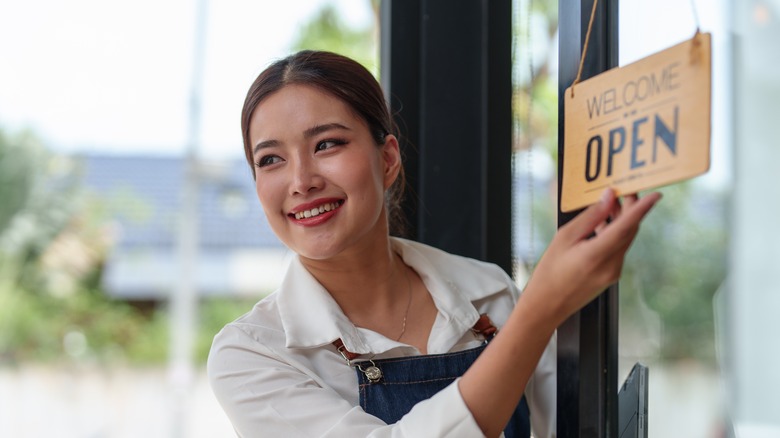 Smiling woman looking to left as she flips sign over to say open