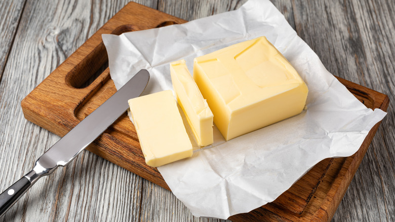An unwrapped and sliced stick of butter sitting on a cutting board with a butter knife