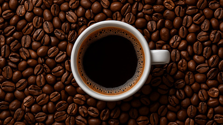 An overhead shot of a mug of black coffee, surrounded by coffee beans