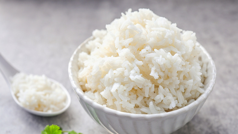 A bowl next to a spoon, both filled with cooked white rice