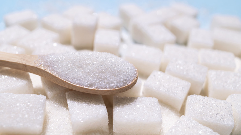 A spoonful of white sugar resting on a pile of sugar cubes