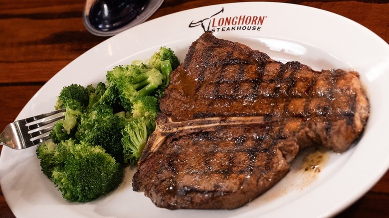 A char-grilled T-bone steak and broccoli on a white plate with a LongHorn Steakhouse logo on it.