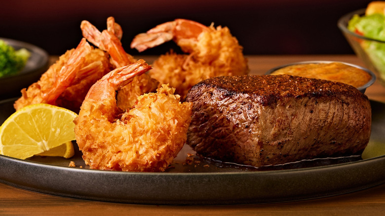 A plate of breaded shrimp with a perfectly seared steak on a wooden table at Outback Steakhouse