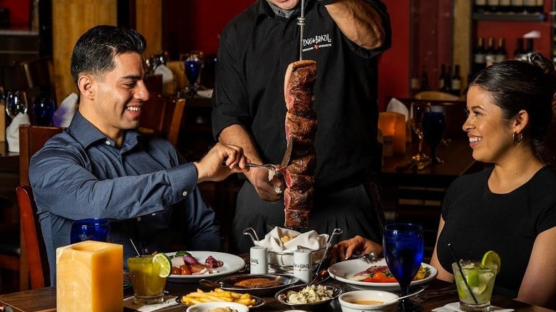 A server carving a large skewer of beef at a table for a couple dining at Texas de Brazil