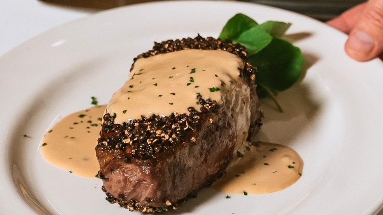 A close-up of a steak on a white plate coated in Bearnaise sauce  being served at The Capital Grille.
