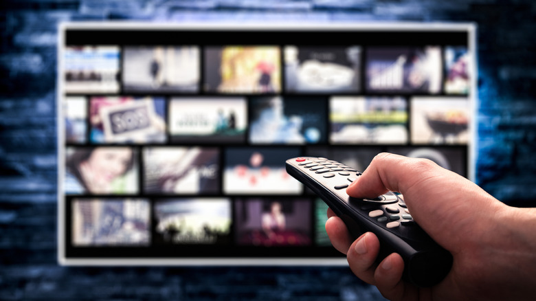 person holding TV remote in front of a streaming screen