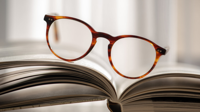 Pair of glasses resting facing camera, on an angle, between pages of open blook