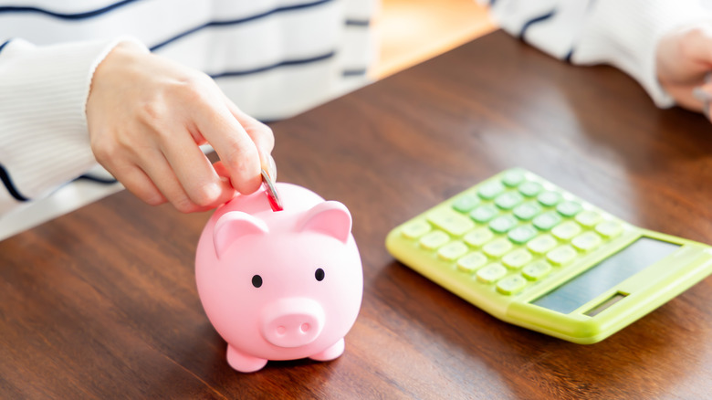 person with calculator putting money in piggy bank