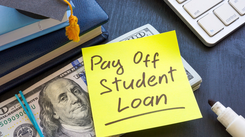 "Pay off student loan" wirtten on a yellow post-it note over $100 bills