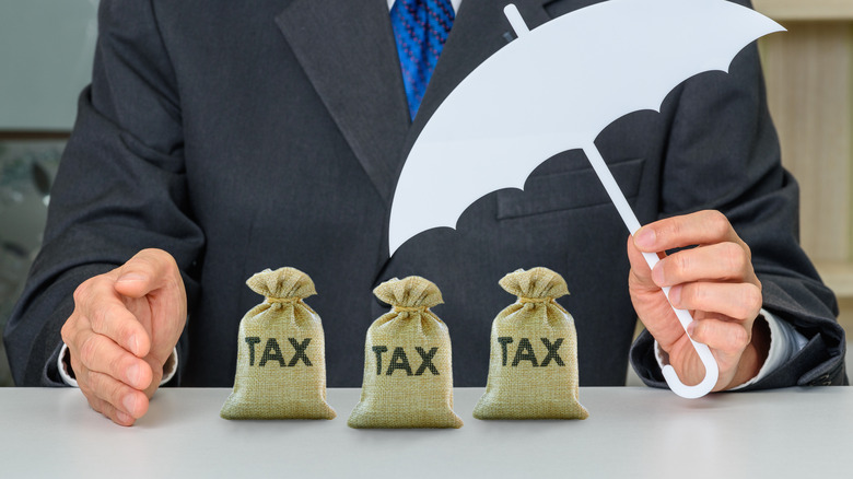 man holding umbrella over bags labeled tax