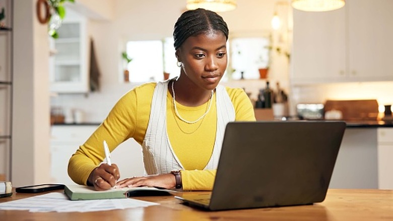 A young woman sits at her kitchen table on a laptop making plans