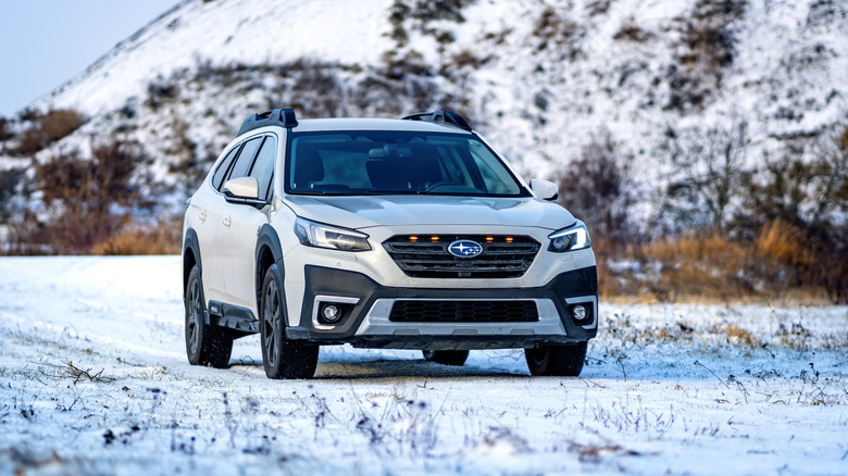 A white Subaru driving on a snow-covered road in the mountains.