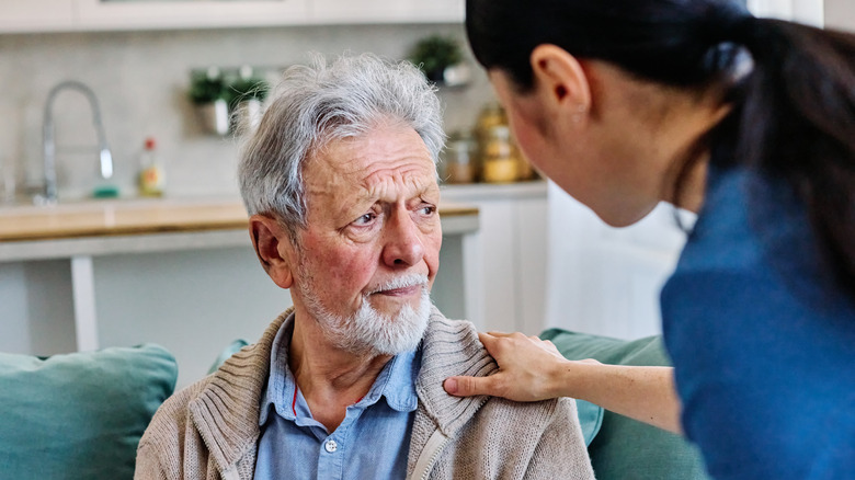 Doctor or nurse caregiver's hand giving support to sad lonely senior man at home or nursing home.