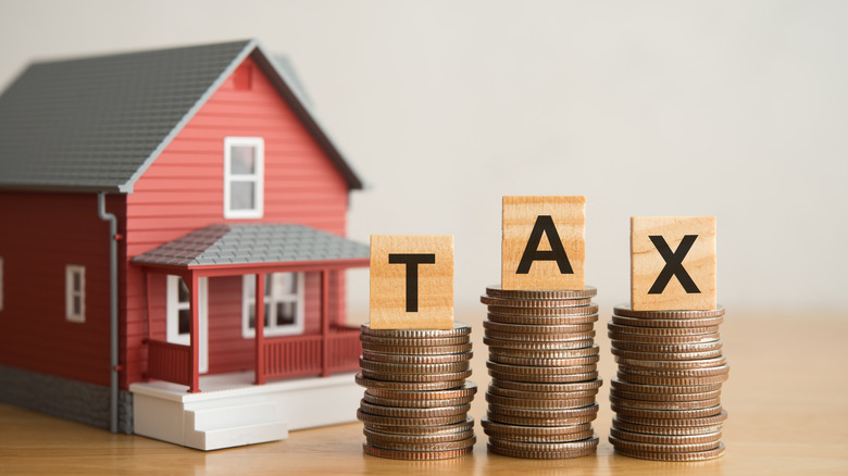 A model house and TAX alphabet on stack coins with white wall background.