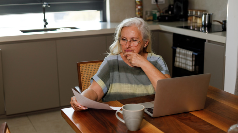 An elderly woman looking concerned as she looks at her taxes.