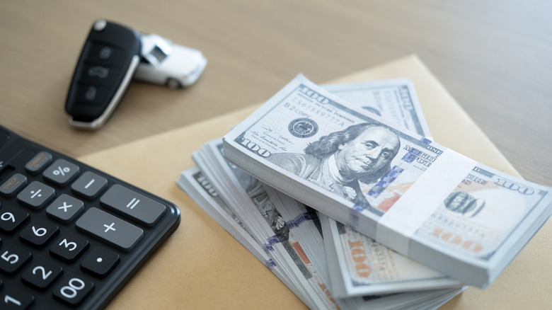 Stacks of dollar bills, car key, and calculator on table showing car loan calculation, finance planning, or vehicle purchase budgeting.