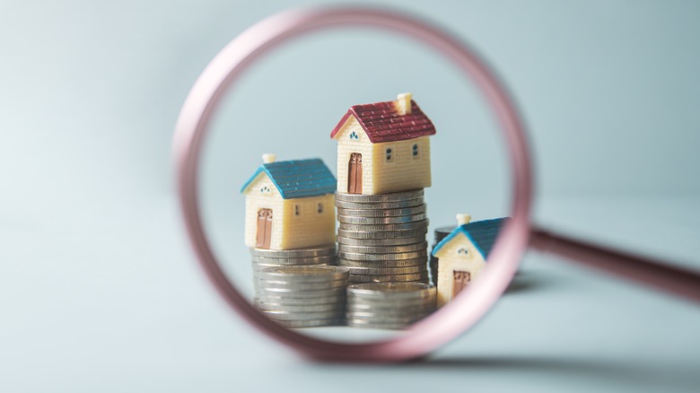 Minature houses sit on stacks of coins as seen through magnifying glass