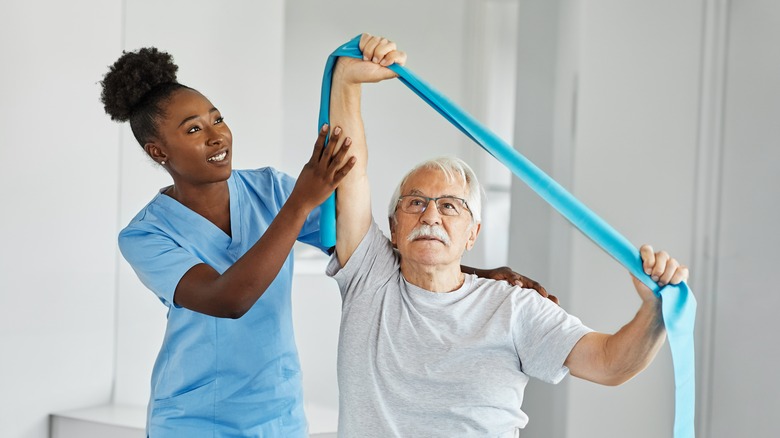 Female nurse helps older male patient to stretch using band