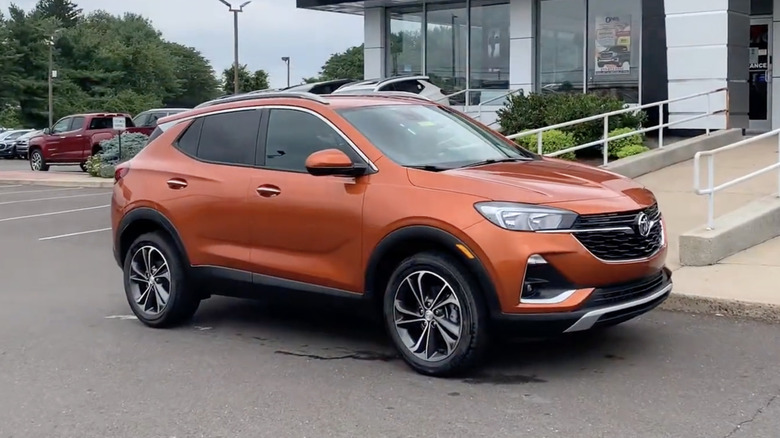 An orange 2022 Buick Encore GX parked in front of a ramp at a dealership's entrance