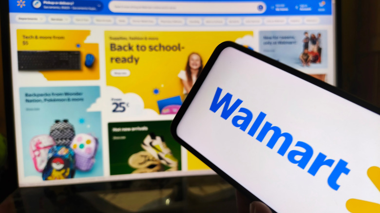 Shot of Walmart logo on smartphone screen with Walmart website on background laptop