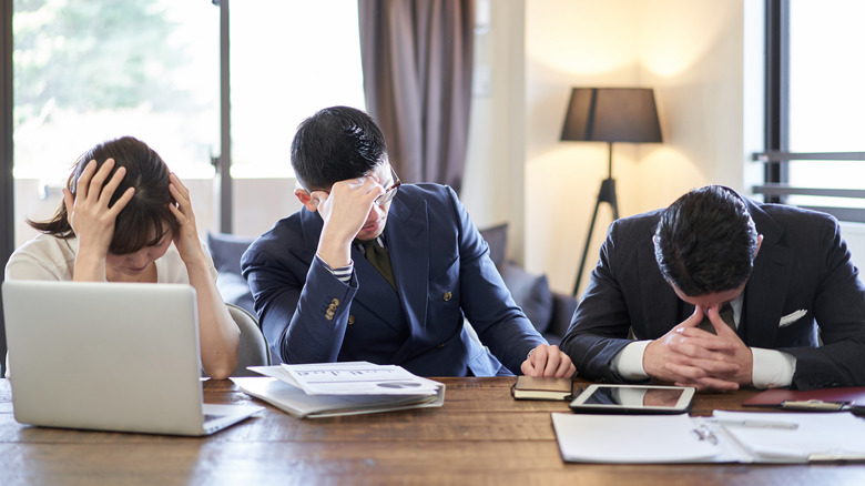 female and two male business colleagues sitting at table hold their heads in despair
