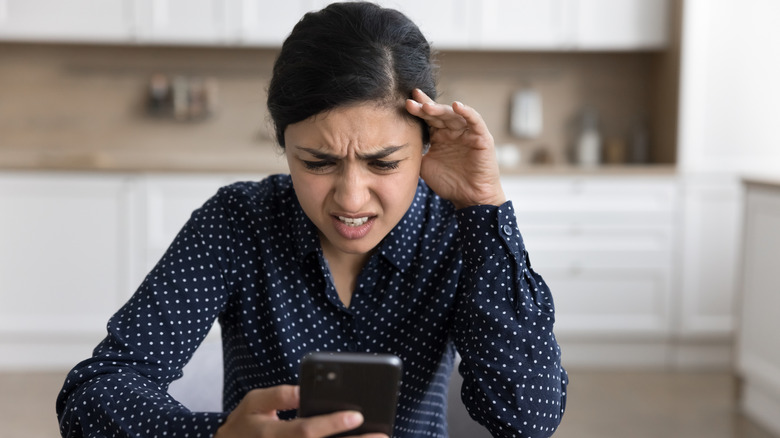 a young woman stares at her cellphone with a look of confusion