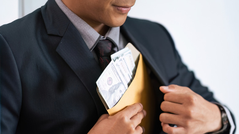 man in blue suit and tie placing envelope full of money in his inner coat pocket