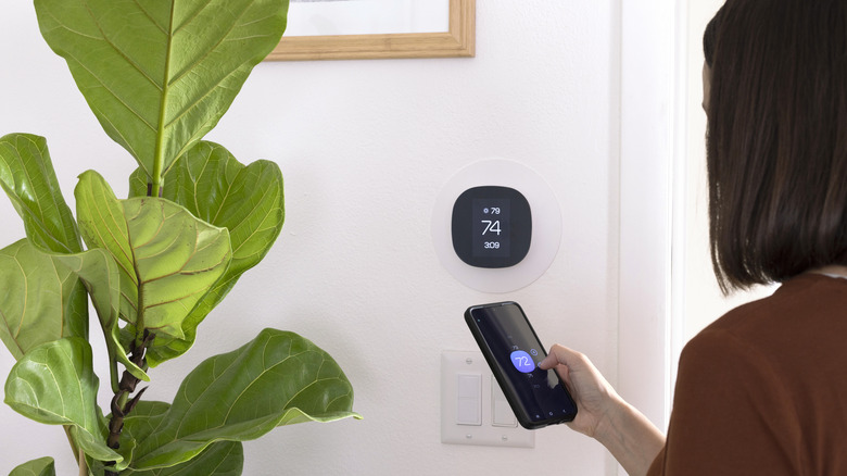 woman holding phone and looking at smart thermostat