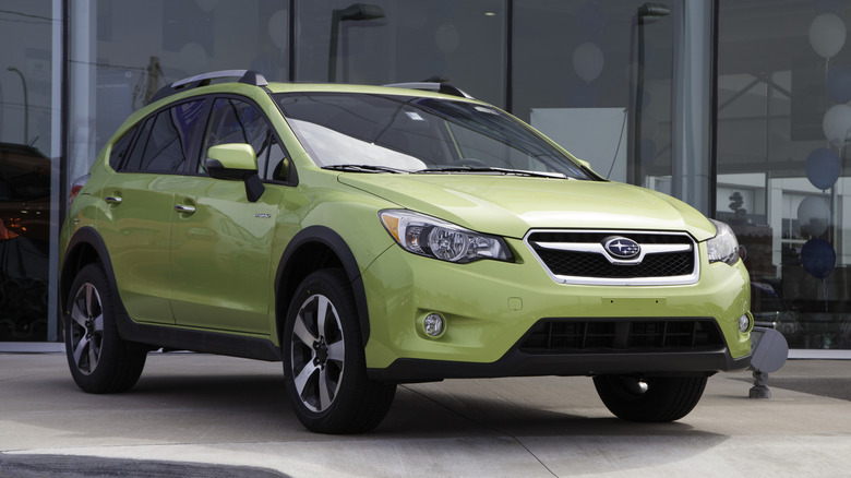 A new Subaru XV Crossover Hybrid sits on display outside and in front of a car dealership showroom.