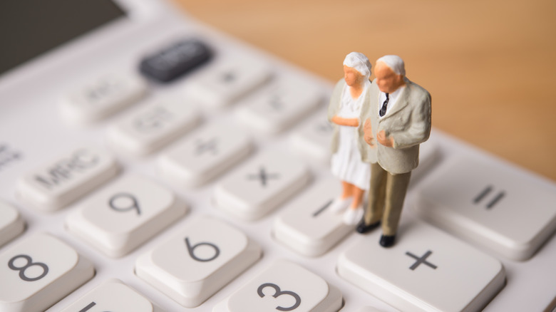 senior figurines standing on a calculator