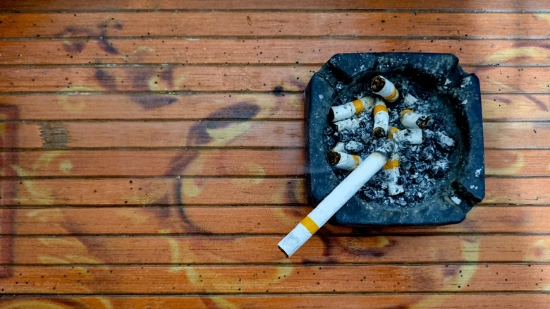 Burning cigarette sitting in black ashtray