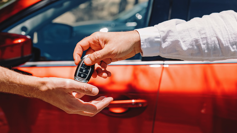 Man with long sleeve shirt placing car keys into open palm of another man with car in background