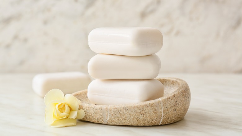 A stack of three bars of soap in asymmetrical brown bowl next to rose