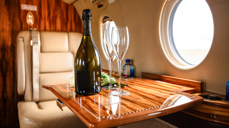 A bottle of win and champagne glasses on tray in the first-class seat of a plane