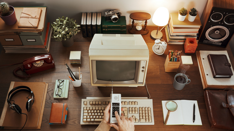 Person pressing buttons on cordless phone in front of 1980s style desk